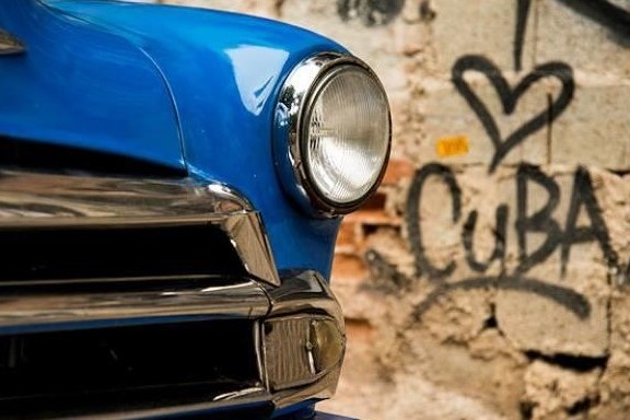 The headlight of a blue car in front of a graffitied wall