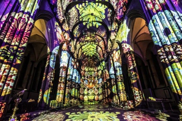Luxmuralis - Colorful abstract patterns projected inside a cathedral with tall arches.