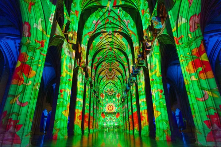 National Cathedral interior with vibrant green and red light projections on arches and columns.